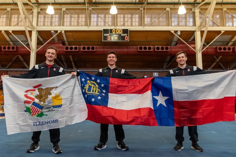 Three gymnasts pose while holding the Illinois, Georgia and Texas state flags.