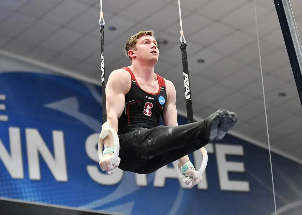 Gymnast Ian Gunther performs on the rings, with a Penn State gym banner partially visible in the background.