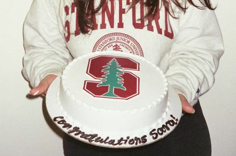 Sara holds a big cake with the Stanford logo on top. The cake reads: "Congratulations Sara!"