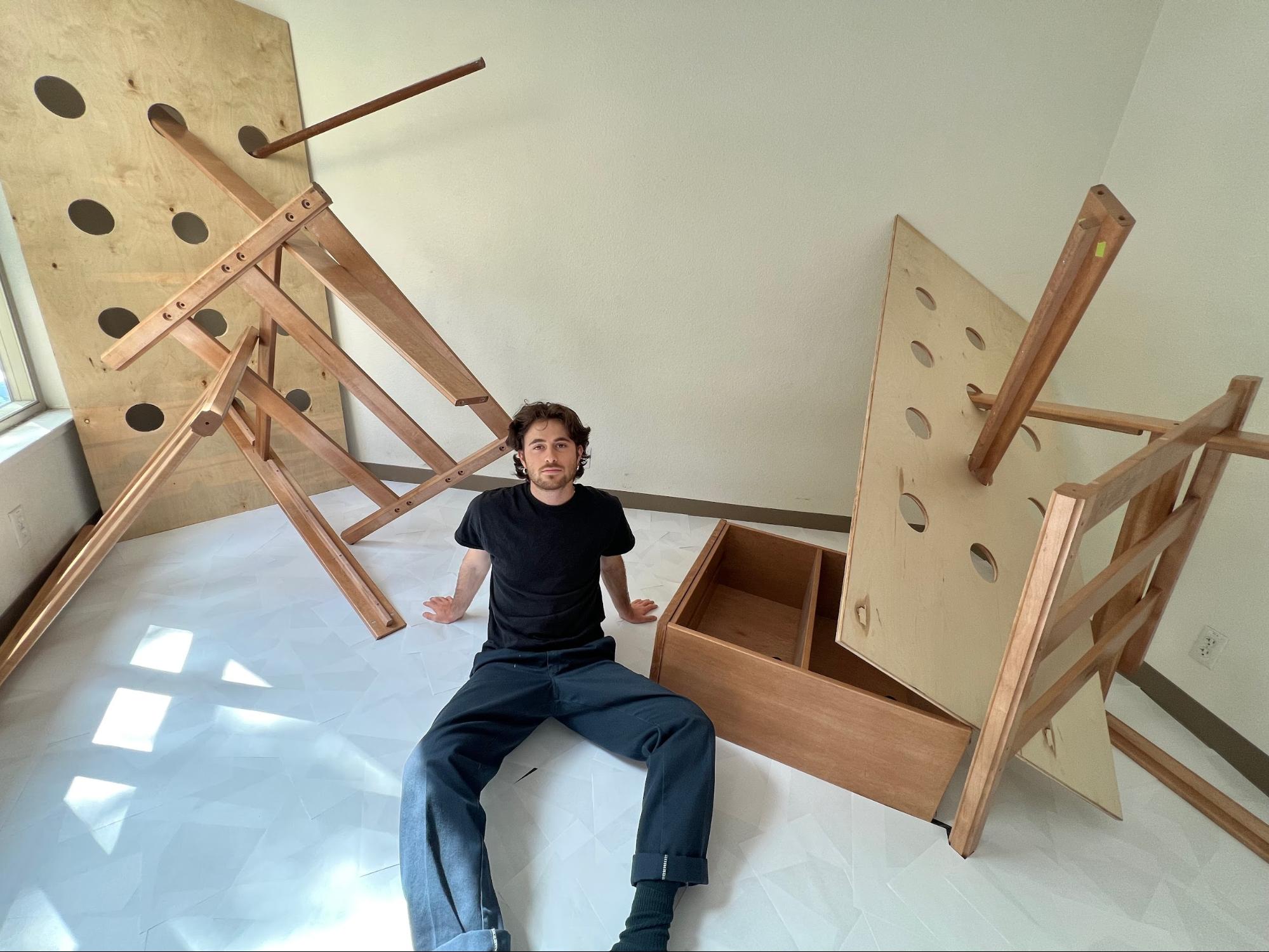 Yonatan Laderman ’23 sits between the reconstructed bed frames that make up his art exhibition, "2: A Monument."