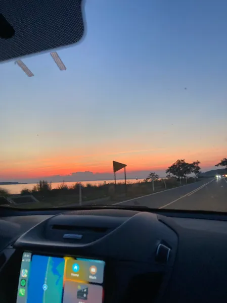 Looking out from inside a car. Driving down the coast. The sun is setting in the distance.