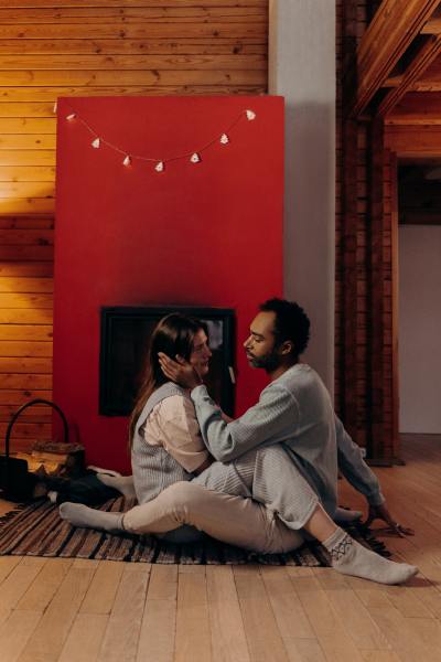 A man and a woman lean in for a kiss in front of a red fireplace.