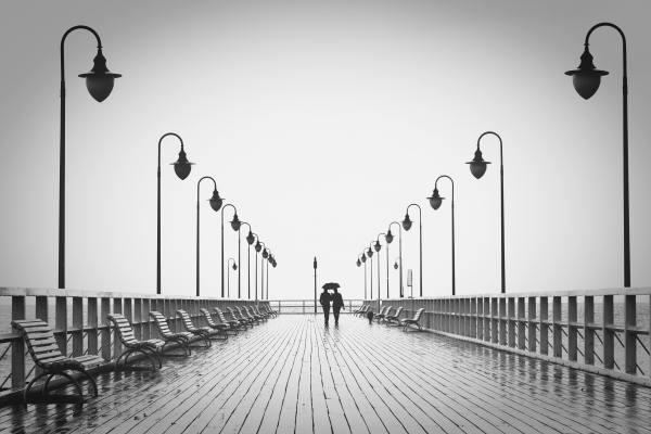 A black and white photo of a couple standing at the end of a pier.