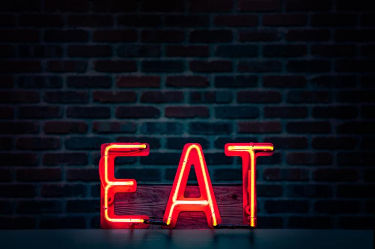 Orange neon letters reading "EAT" framed against a brick wall.