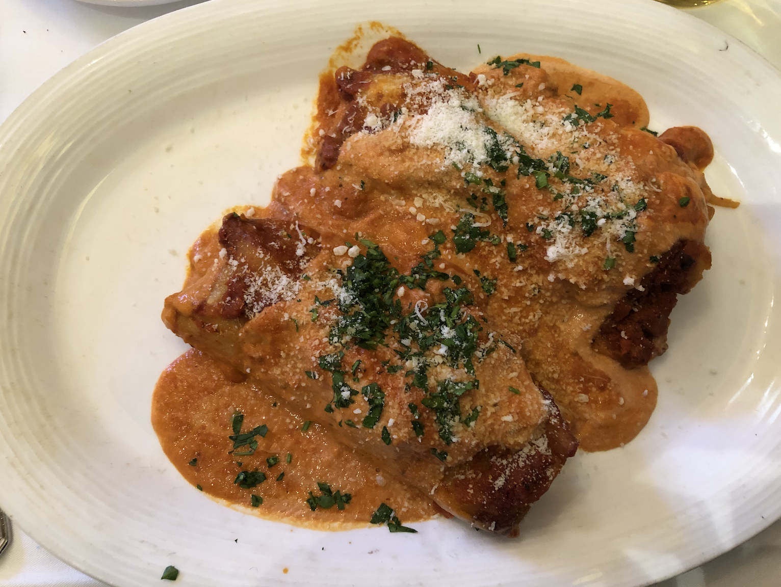 The cannelloni is served with two pieces of stuffed pasta, garnished with cheese, sauce and chopped herbs.
