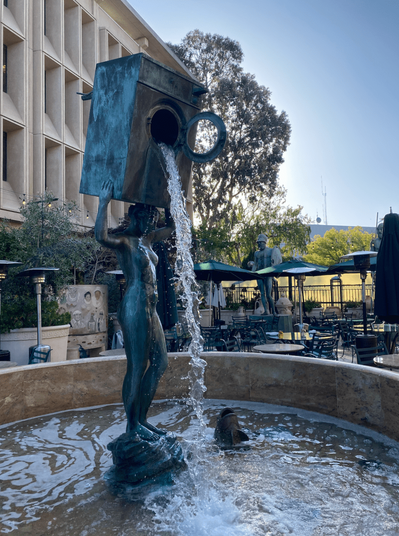 A fountain featuring a woman holding a washing machine from which water spills stands in front of Cafe Riace.