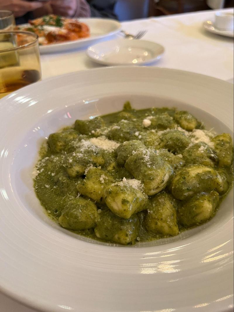 The pesto gnocchi sits in a white dish with Parmesan cheese on top.