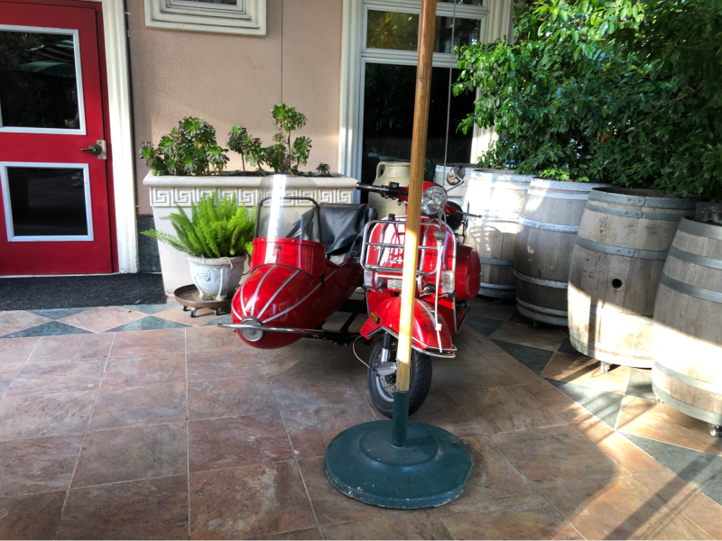 A red vespa with a side car sat outside of Caffe Riace under a sun umbrella.