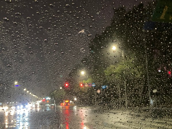 Looking through a rain-splattered windshield. it is dark outside, and the streetlamps all blur together.