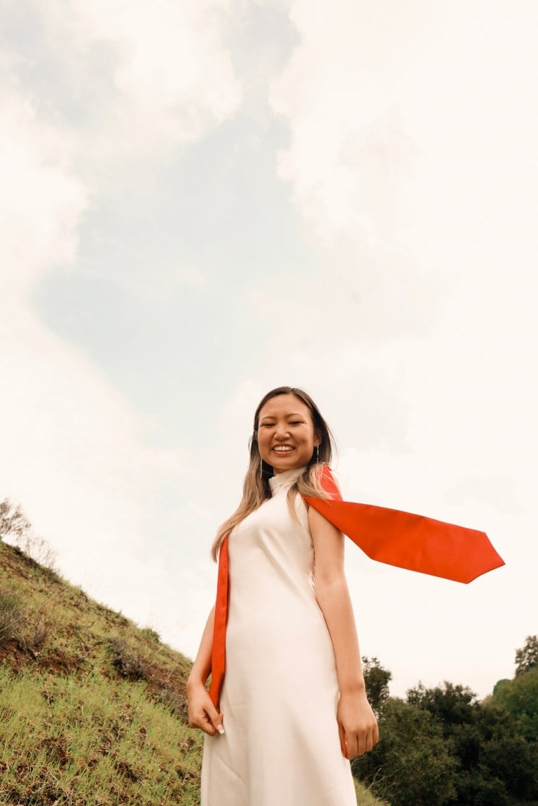 A person stands in a white dress with a red Stanford stole blowing in the wind.