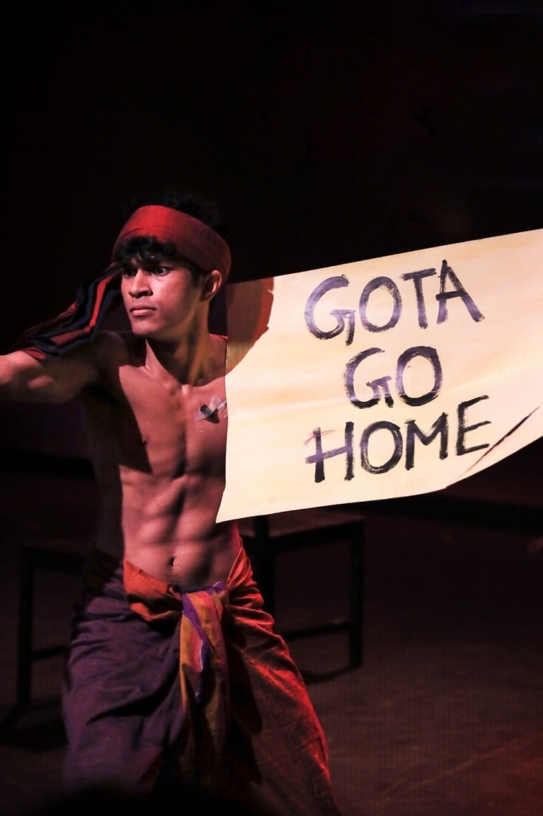 Leeth Singhage, with his upper body naked, holding a banner that says "Gota Go Home."