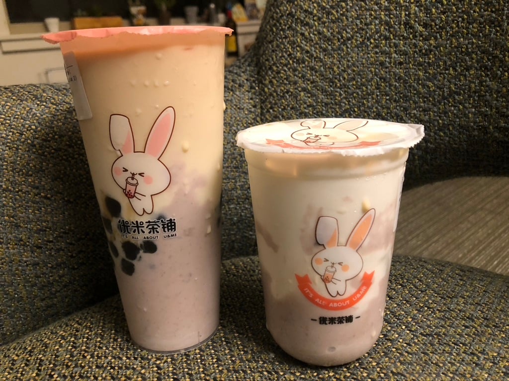 One large and one small boba drink from Ume Tea sit on a couch, each with a cartoon bunny drinking boba decorating the cup.