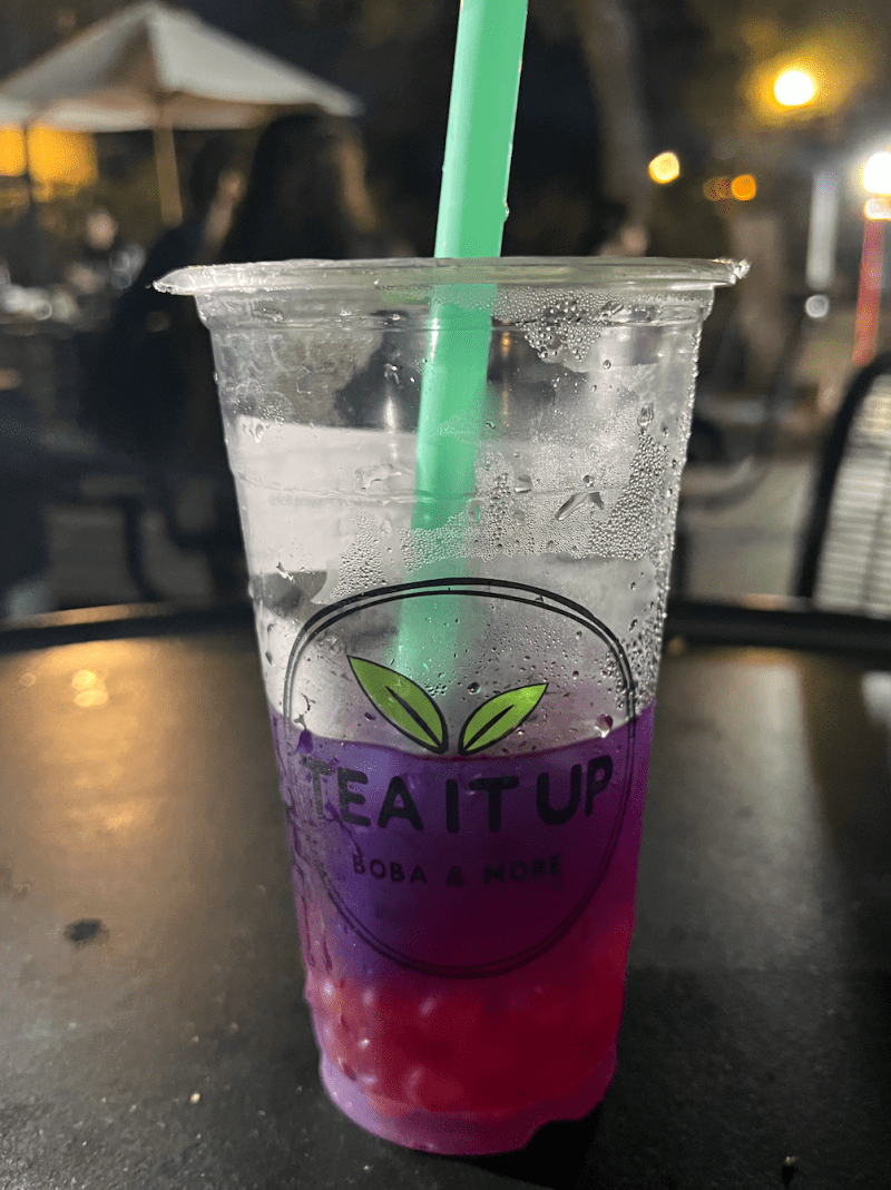 A pretty purpose Lavender Love boba drink from Tea it Up sits half-finished on a black table. 