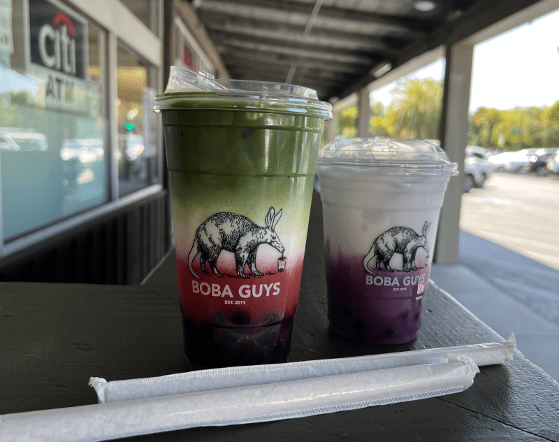 The strawberry matcha latte and ube latte drinks from Boba Guys sit on a table outside in Town and Country.