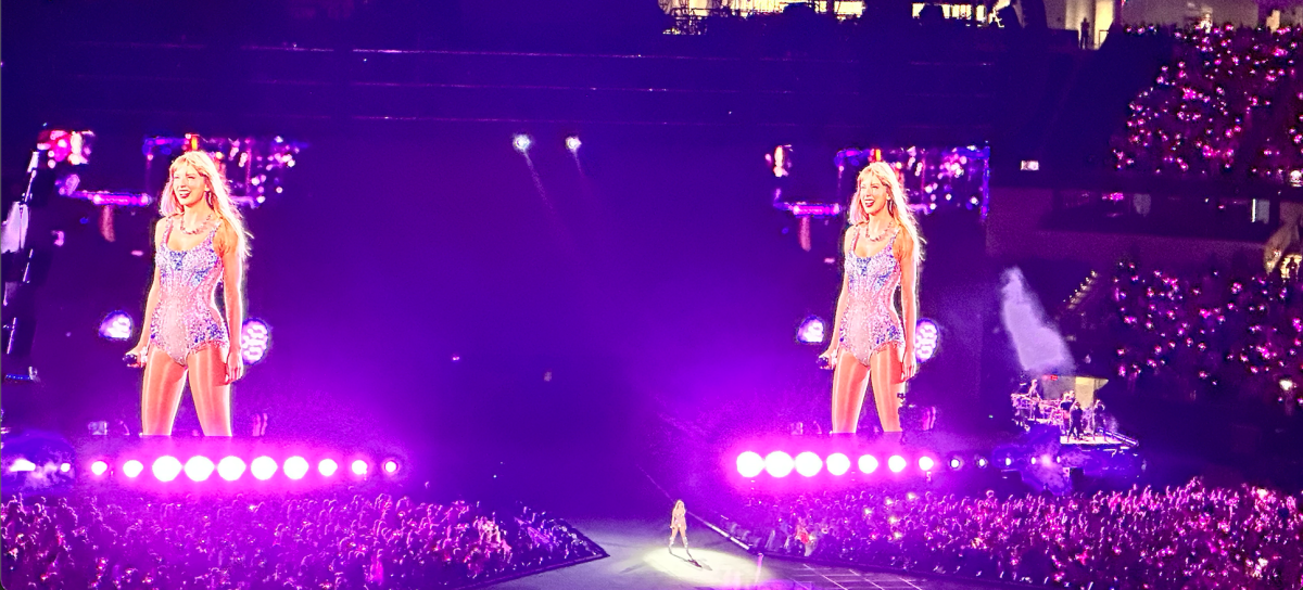 Taylor Swift sings on stage. In the background are two projections of her live image.