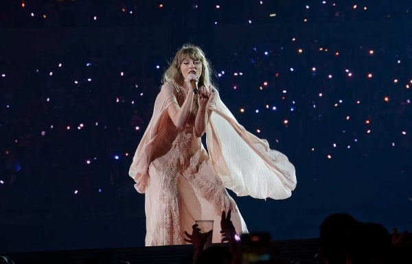Taylor Swift singing to the audience against a black backdrop.