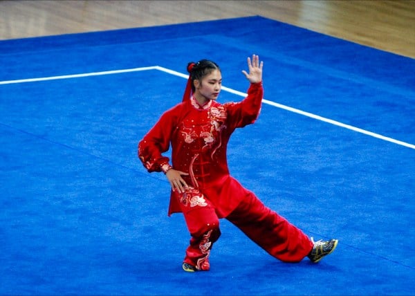 An athlete in a tai chi stance on a blue mat.
