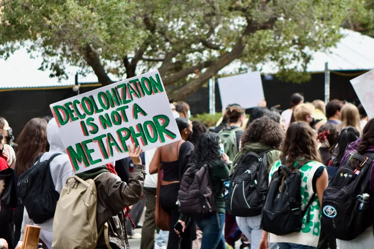 Hundreds of students gather in protest while holding pro-Palestine signs.