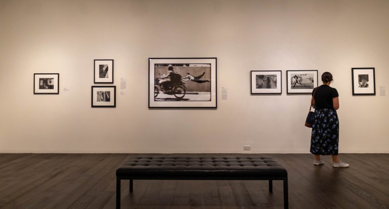 A woman stands facing a white wall with seven black and white photographs of varying sizes.