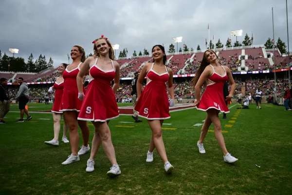 The Dollies dressed in the classic red and white uniform smile at the crowd from the side of the football field while in a pyramid formation.