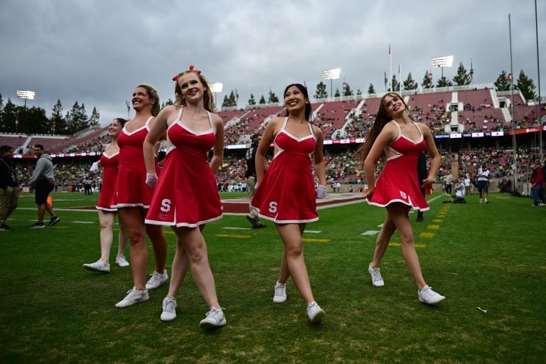 The Dollies dressed in the classic red and white uniform smile at the crowd from the side of the football field while in a pyramid formation.