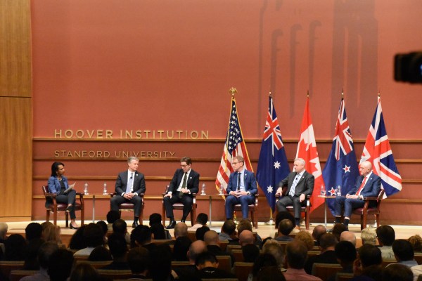 Condoleeza Rice sits on stage with representatives from the Five Eyes in front of their countries' flags.