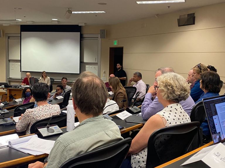 A room full of seated professors, each with a microphone in front. They face Jenny Martinez, who leads discussion from the front of the room.