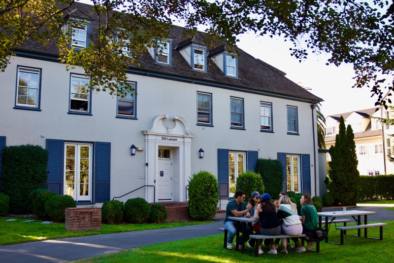 Students sit at a picnic table outside the 550 Lasuen house, formerly the Sigma Chi fraternity house.