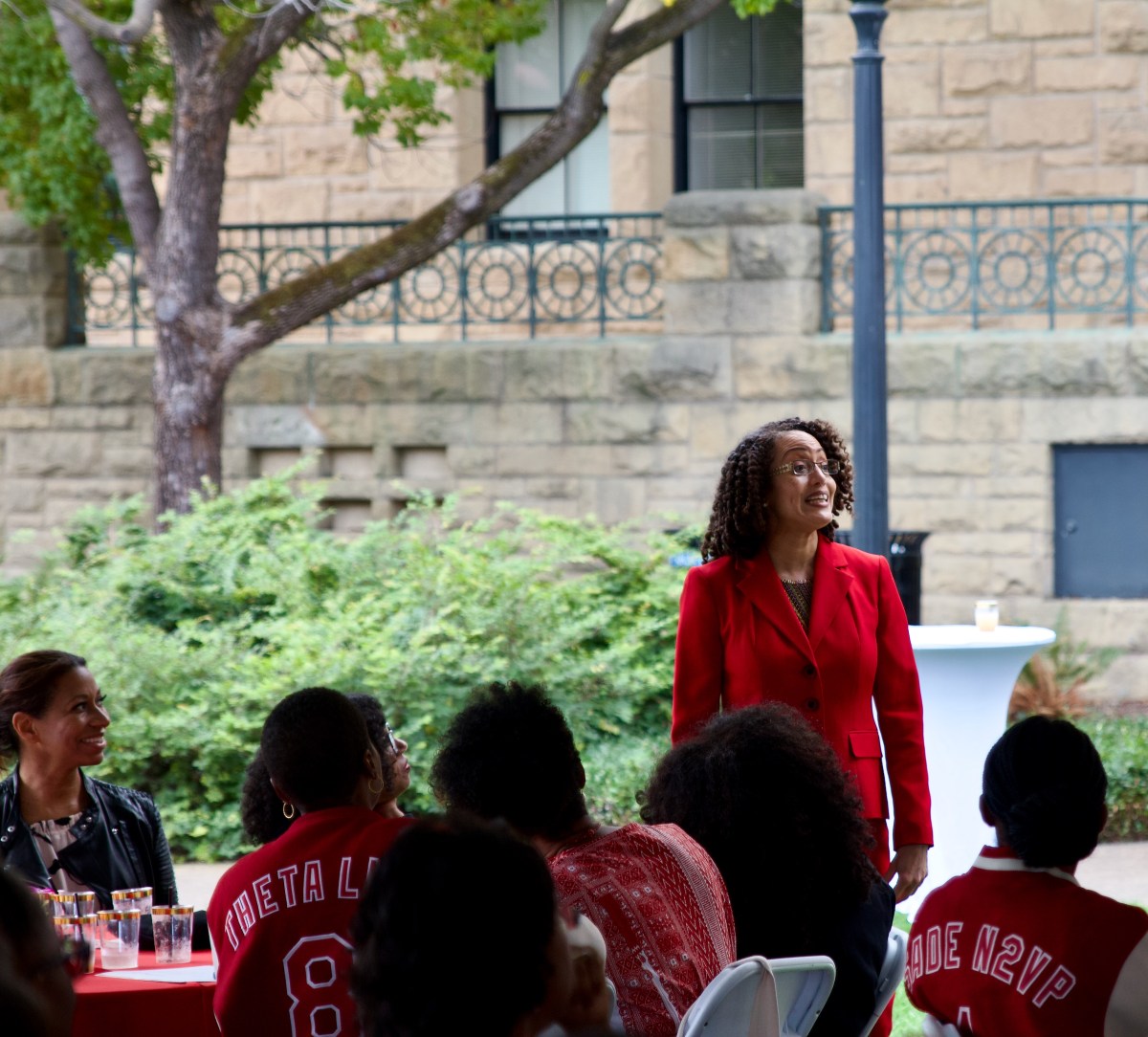 Stacey Dixon '93 wearing a red blazer stands and speaks to the guests.