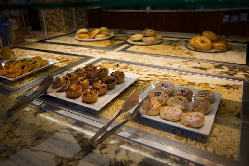 A spread of muffins, bagels, and danishes with tongs.