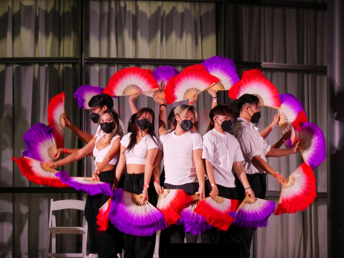 A group of dancers wearing black masks and holding magenta fans.