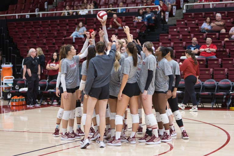 Players in a huddle with hands raised towards a volleyballl.