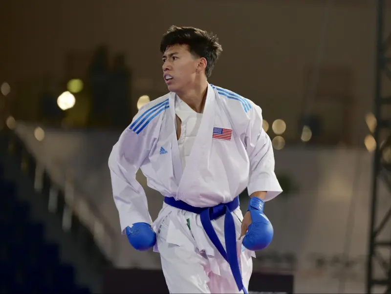 Athlete in blue gloves and karate uniform turned to the side.