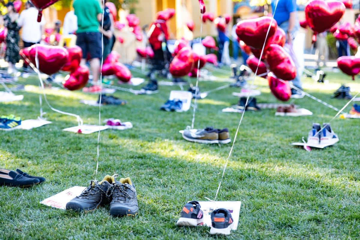 Shoes tied to red heart balloons. Posters next to the shoes with information about hostages. 