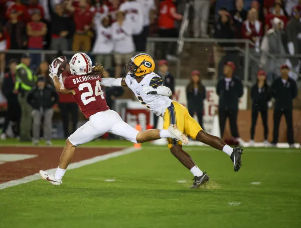 A Stanford player lunges to catch the football at the end zone while a Berkeley defender reaches behind him.