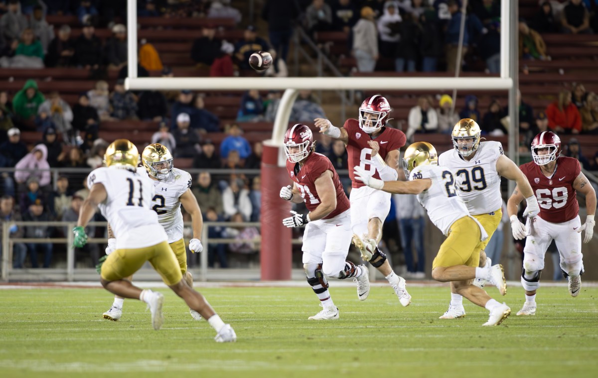 Stanford's quarterback throws the ball, midair, to a receiver. Notre Dame defenders close in.