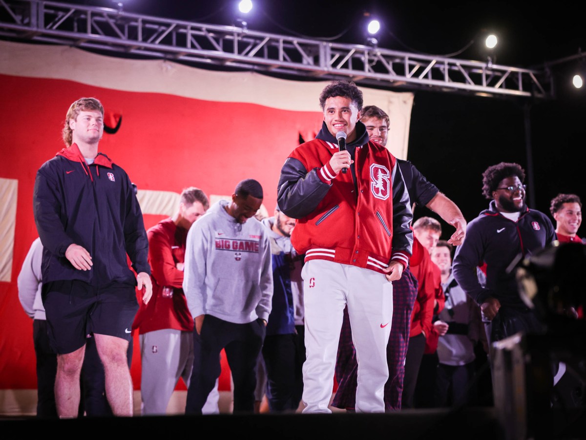 A student-athlete holds a microphone on stage in front of his team. All are smiling.