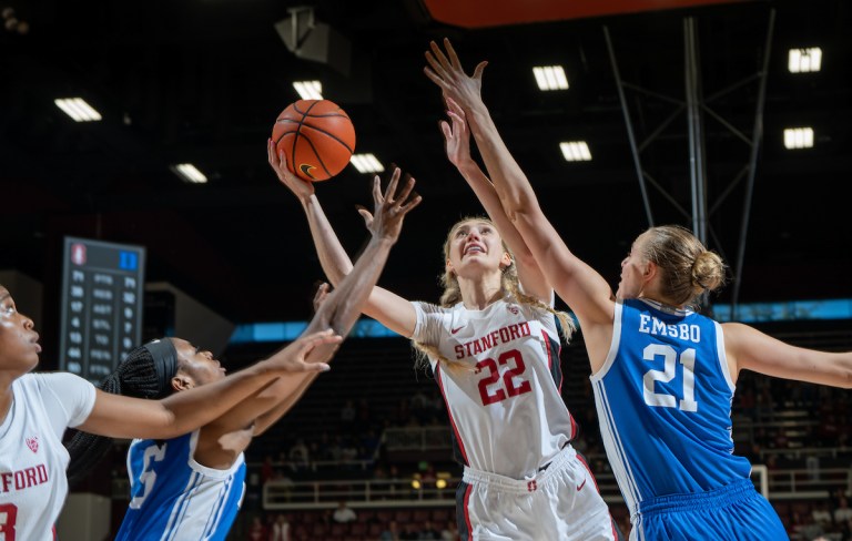 A player extends her arm toward a basketball as two other people jump up.