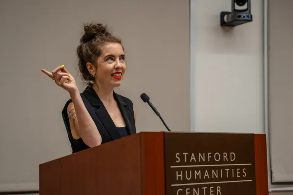 Writer Emily Geminder talks behind a rostrum which reads "Stanford Humanities Center".