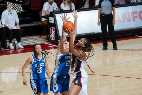 A Stanford player jumps above two Duke players to grab the ball.
