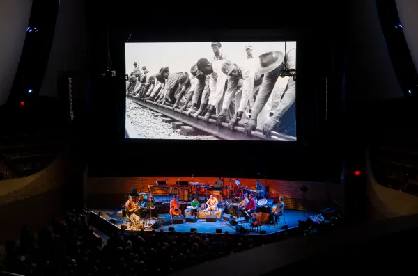 Members of the Silkroad Ensemble perform in front of a backdrop depicting African American men working on constructing the American Railroad during the emsemble's concert in Bing Concert Hall.