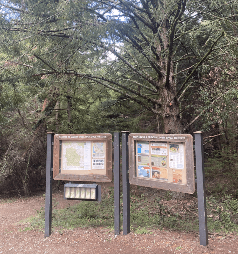 Two sign posts describing trail routes with trees in the background.
