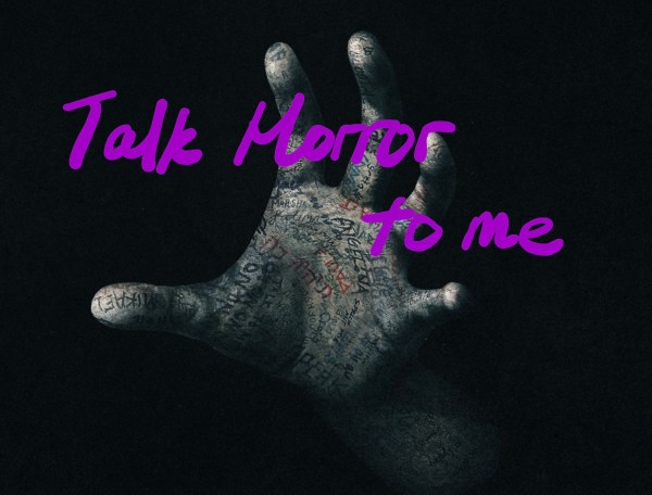 The photo of a hand in the dark, with the text "Talk Horror to me" written in the foreground.