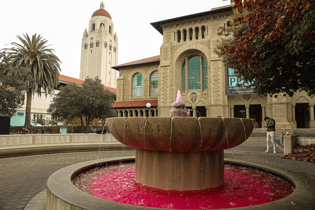 The fountain in front of Green Library running with red water. Hoover Tower sits in the background.