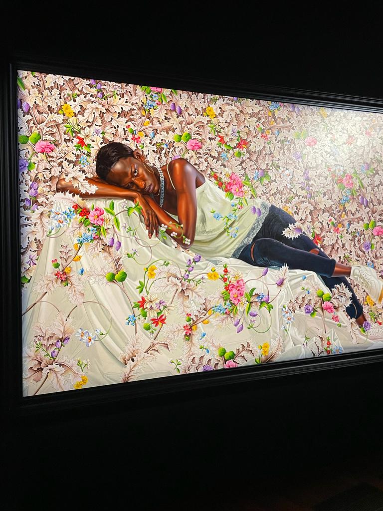 Painting of a black woman lying on white sheet and surrounded by flowers.