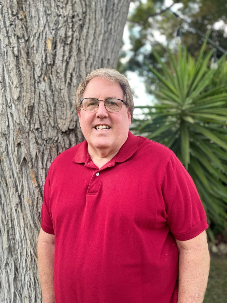 Jason Cole '84 poses in front of tree in a red shirt