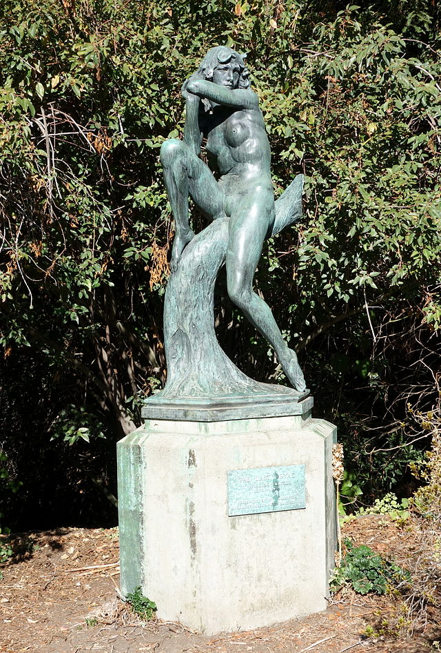 A sculpture of a female figure perched on a branch.