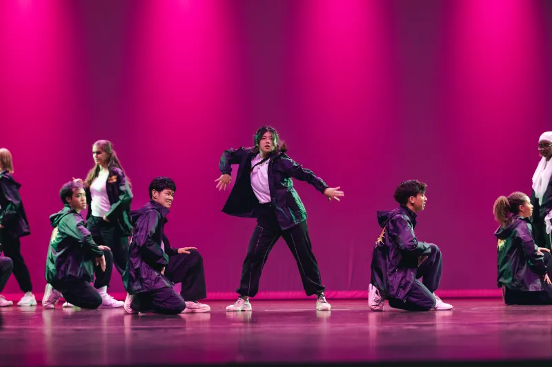 A group of dancers in black dancing on stage.