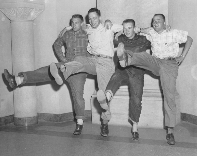 Four men smiling doing a kickline