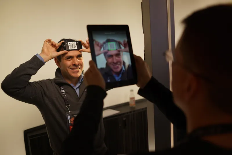 Daniel Lubetzky poses with a QR code on his head while another person scans the code with a tablet camera.